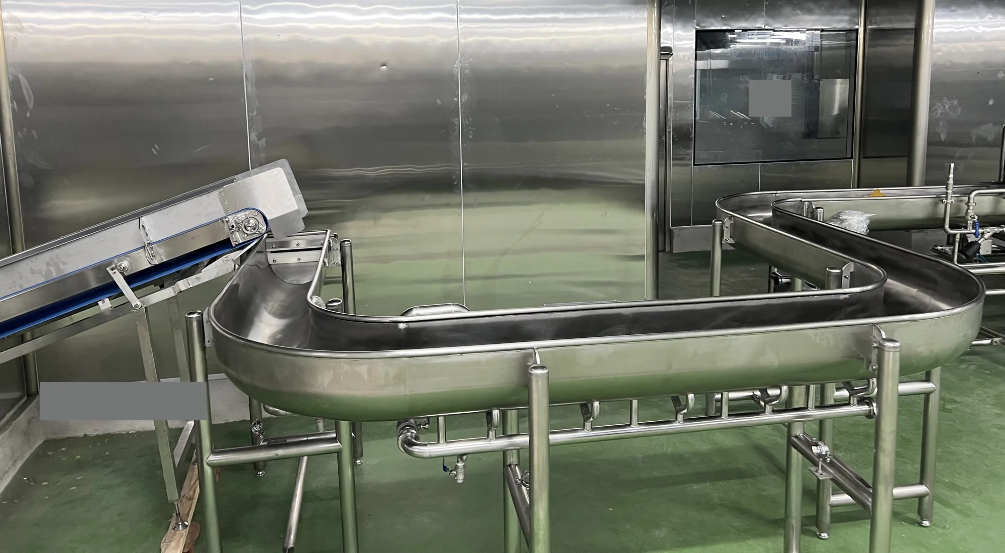 Curved stainless steel processing channel beside an inclined conveyor